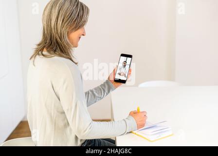 Patiente sénior utilisant une application mobile pour la communication vidéo avec un médecin indien.Femme âgée à cheveux gris avec smartphone parlant en ligne avec un thérapeute.Concept de télémédecine Banque D'Images