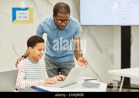 Portrait d'un jeune enseignant afro-américain qui aide une adolescente dans une salle de classe moderne, espace de copie Banque D'Images