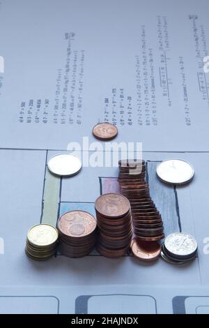 Colonnes de pièces à côté d'un graphique à barres sur un livre blanc avec équations.L'une des colonnes est en bas.Copier l'espace.Mise au point sélective.Photographie verticale. Banque D'Images