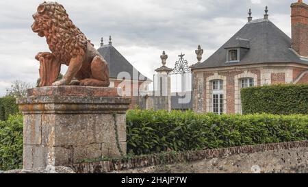 Une statue d'un lion s'assit sur un plynthcontre un ciel bleu et donne sur un jardin de château Banque D'Images