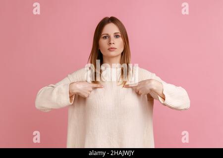 Portrait de blonde haughty femme pointant vers elle-même et regardant avec arrogance à la caméra, étant fier et égoïste, portant chandail blanc.Studio d'intérieur isolé sur fond rose. Banque D'Images