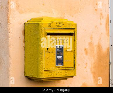 Une boîte aux lettres postale française jaune est accrochée à un mur de maison ocre à Tourtour, dans le département du Var, en France. Banque D'Images