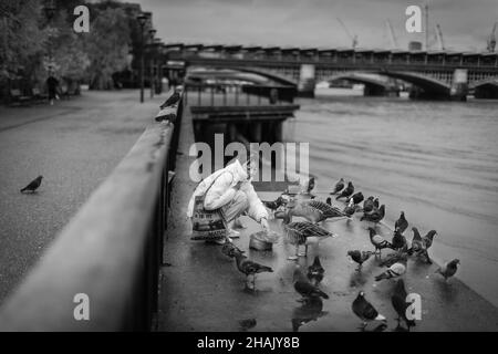 Une femme qui nourrit les oiseaux sur la rive sud près du pont de Blackfriars à Londres. Banque D'Images