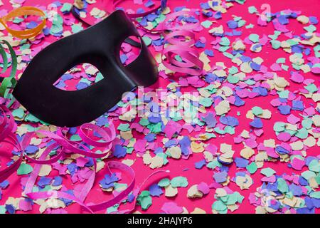 Carnaval confetti fond festif.Masque noir et cercles de papier colorés et lumineux sur rose.Modèle d'invitation à une fête Banque D'Images