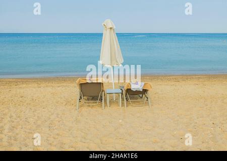 Vue incroyable sur deux chaises longues vides et parasol sur la plage près de l'eau.Grèce. Banque D'Images