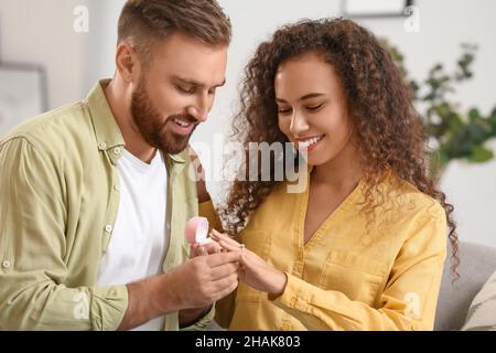 Jeune homme mettant l'anneau d'engagement sur le doigt de sa petite amie à la maison Banque D'Images