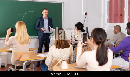 Professeur de mathématiques donnant des conférences aux étudiants adultes en auditorium, expliquant le graphique de fonction sur le tableau noir Banque D'Images