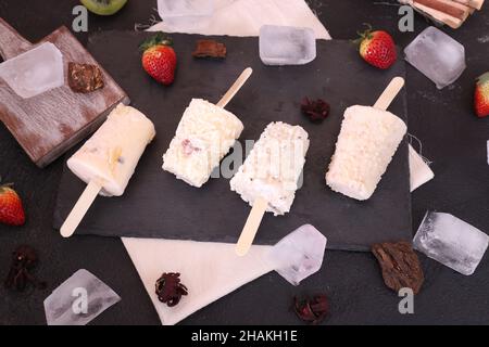 Des popsicles faits maison aux saveurs différentes sur la table noire avec des fraises et des glaçons Banque D'Images