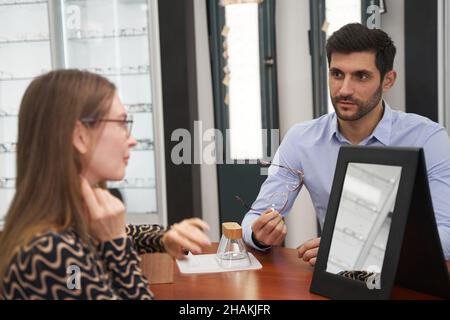 Un travailleur de l'atelier d'optique donne des explications au client au sujet des lunettes Banque D'Images