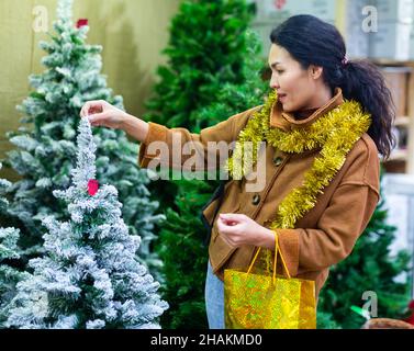 Une femme asiatique heureuse choisit un arbre de Noël sur le marché de rue Banque D'Images