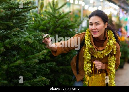 Une femme asiatique heureuse choisit un arbre de Noël sur le marché de rue Banque D'Images