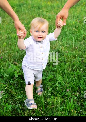 La main des parents et l'enfant première étape.Bébé jouant dans l'herbe verte.Enfant s'amusant sur un pique-nique en famille dans le jardin d'été.Portrait d'une jeune famille heureuse Banque D'Images