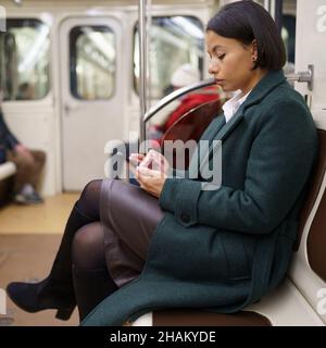 Femme afro-américaine fatiguée employée de bureau avec smartphone dans le métro, se rentrent après le travail Banque D'Images