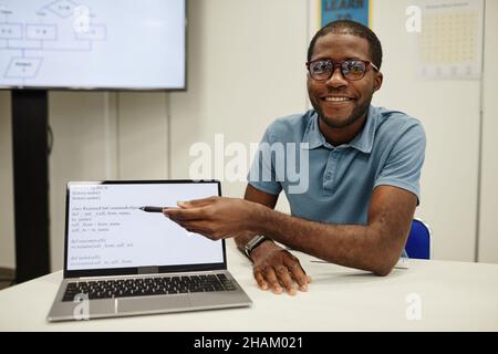 Portrait d'un jeune enseignant noir pointant vers l'écran d'ordinateur portable dans la classe de codage pour les enfants, espace de copie Banque D'Images