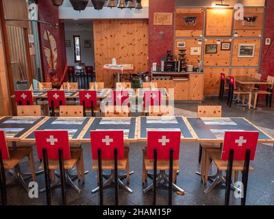 Gruyères, Suisse - 23 novembre 2021 : intérieur d'un restaurant suisse typique à Gruyères avec chaises et drapeau suisse à l'arrière. Banque D'Images