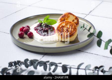 Crêpes au fromage cottage, syrniki aux baies fraîches et confiture pour le petit déjeuner sur carreaux à l'eucalyptus Banque D'Images