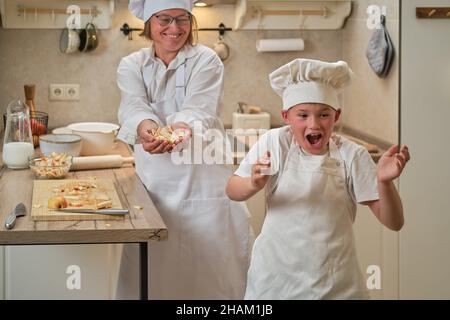 Mère et fils cuisant une tarte aux pommes dans la cuisine. Une femme et un garçon dans des chapeaux de chef et des tabliers cuisinent avec des pâtisseries Banque D'Images