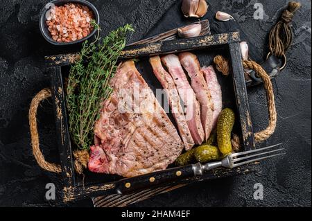 Rôtis sur des steaks de porc grillés à la viande de cou dans un plateau en bois aux herbes.Arrière-plan noir.Vue de dessus Banque D'Images