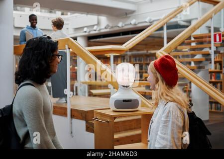 Étudiants utilisant l'assistant vocal dans la bibliothèque Banque D'Images