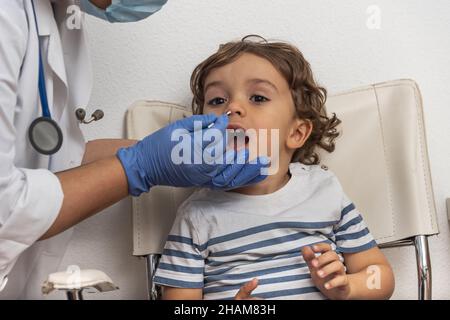 Médecin prenant un écouvillon pour un échantillon de virus corona provenant de la bouche d'un garçon caucasien potentiellement infecté.Test de laboratoire Covid-19.personnel médical avec test de combinaison PPE Banque D'Images