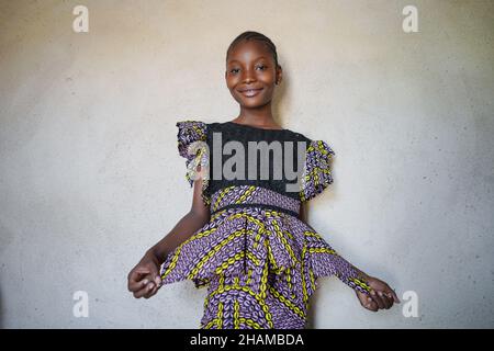 Portrait Jeune belle fille africaine sourire et poser avec la robe traditionnelle colorée par fond de mur vierge Banque D'Images