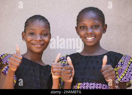 Portraits de deux jeunes filles afro-américaines souriantes montrant les pouces avec un arrière-plan mural vierge Banque D'Images