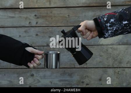 Un homme verse du café pour un homme à partir d'une cafetière dans une tasse en métal. Un homme verse du café d'une cafetière dans une tasse en métal pour un autre homme en plein air Banque D'Images