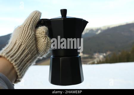 La main dans la mitaine maintient la cafetière contre les montagnes Banque D'Images