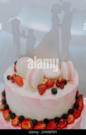 Un gâteau de mariage traditionnel et décoratif à la réception de mariage. Un gâteau de mariage blanc sur plusieurs niveaux sur une base argentée et des fleurs roses sur le dessus.Image d'un Banque D'Images