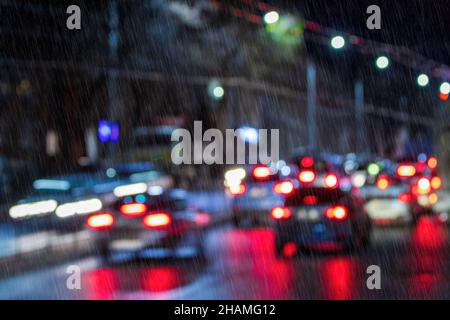 Des lumières floues de voitures et de lanternes en mouvement réfléchissantes sur l'asphalte humide dans la ville de nuit sous la pluie.Concept de mauvais temps pluvieux. Banque D'Images