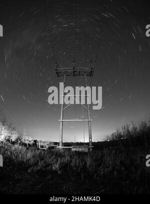AIRDRIE, CANADA - le 17 novembre 2021 : une prise de vue verticale en niveaux de gris d'une tour d'électricité sous un ciel nocturne avec des pistes étoiles Banque D'Images