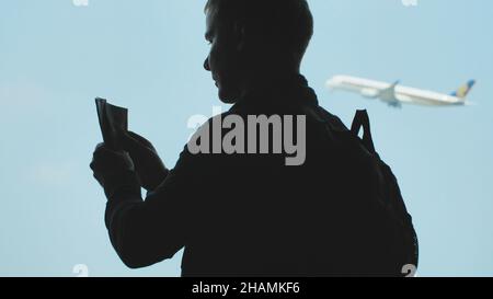 Silhouette d'un jeune homme compte dollars contre l'arrière-plan d'un avion au décollage. Banque D'Images