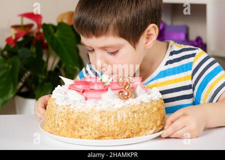 Un enfant de 3 ans mange un gâteau d'anniversaire, léche la crème du dessus assis à la table Banque D'Images