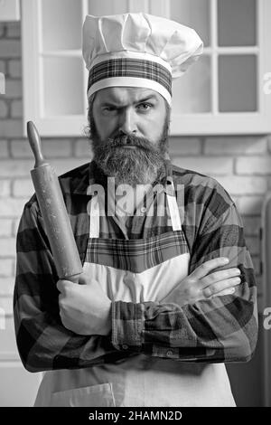 Cuisinier barbu en colère dans un tablier avec une goupille élastique, un portrait sur le fond de la cuisine. Banque D'Images