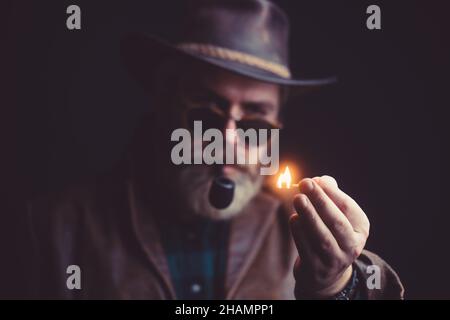 Guy fume le tuyau de tabac. Taille basse avec barbe et moustache sur un visage sérieux. Banque D'Images