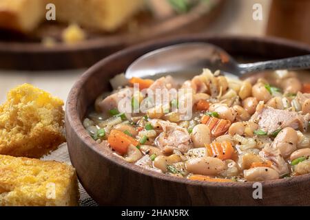 Soupe au jambon et aux haricots avec carottes et ciboulette dans un bol en bois avec pain de maïs sur une table rustique en bois Banque D'Images