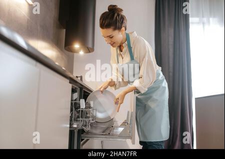 Femme se tenant près du lave-vaisselle et en sortant les plaques Banque D'Images