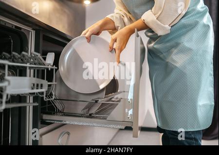 Femme se tenant près du lave-vaisselle et en sortant les plaques Banque D'Images