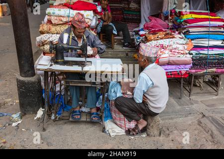 Un tailleur népalais rase un tissu coloré sur une machine à coudre à pédale dans son magasin dans la rue à Katmandou, Népal. Banque D'Images
