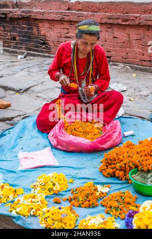 Une femme népalaise enchaîne des fleurs pour faire des guirlandes pour des offrandes religieuses dans les temples hindous de Katmandou, au Népal. Banque D'Images