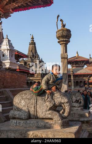 Un jeune garçon népalais sur une statue d'éléphant devant le temple de Harishankar sur la place Durbar, Patan, Népal.Derrière se trouve le Roi Yoganarendra Malla C. Banque D'Images