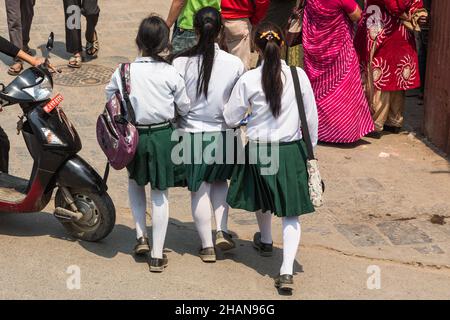 Trois adolescentes népalaises vêtus d'uniformes scolaires marchent de bras en bras sur la place Durbar dans la ville médiévale de Patan, au Népal. Banque D'Images