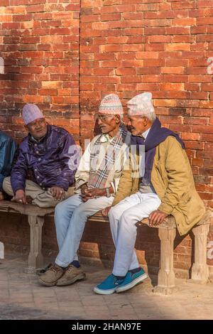 Trois hommes népalais plus âgés portant des chapeaux topi traditionnels de dhaka s'assoient sur un banc dans l'historique place Durbar à Patan, au Népal. Banque D'Images