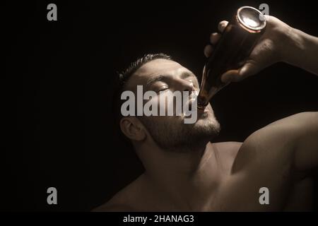 Le style musclé aime le goût de la bière artisanale. Photo de studio sur fond sombre. Banque D'Images