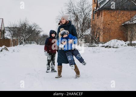 Activités familiales en plein air pour des vacances d'hiver.Une mère heureuse et deux fils jouant des boules de neige dans la rue enneigée de la banlieue.Bonne famille en hiver Banque D'Images