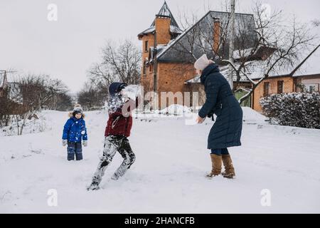 Activités familiales en plein air pour des vacances d'hiver.Une mère heureuse et deux fils jouant des boules de neige dans la rue enneigée de la banlieue.Bonne famille en hiver Banque D'Images