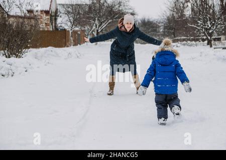 Activités familiales en plein air pour des vacances d'hiver.Une mère heureuse et deux fils jouant des boules de neige dans la rue enneigée de la banlieue.Bonne famille en hiver Banque D'Images