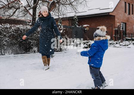 Activités familiales en plein air pour des vacances d'hiver.Une mère heureuse et deux fils jouant des boules de neige dans la rue enneigée de la banlieue.Bonne famille en hiver Banque D'Images