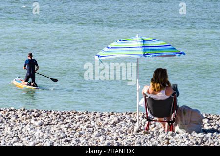 Saint-Valery-en-Caux (nord de la France) : paddleboard et femme assise sous un parasol sur la plage de galets Banque D'Images