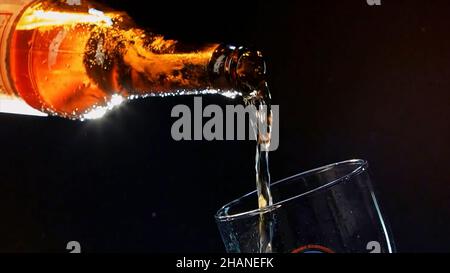 Gros plan du versement de la bière de la bouteille de verre brun dans le verre.Vidéo.Verser la boisson alcoolisée isolée sur fond noir, concept de fête Banque D'Images